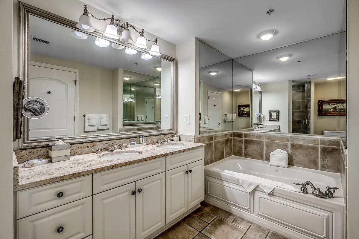 A spacious en-suite bathroom with a double vanity sink, bathtub, and mirrored walls. The space is designed for relaxation, offering a spa-like experience for guests to enjoy at the end of the day.