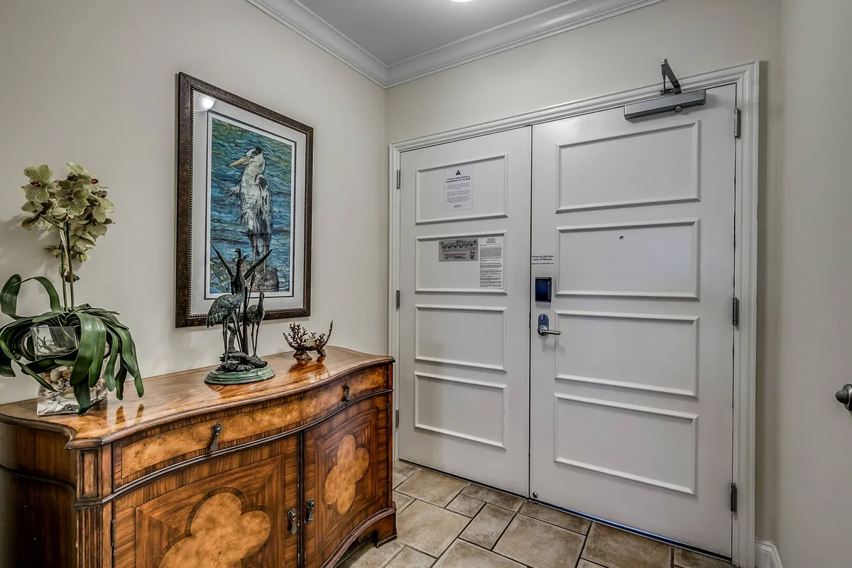The photo captures the condo's entryway, featuring a console table with decorative items, a lush plant, and artwork of a heron, creating a warmly inviting first impression for arriving guests. This area sets the tone for the sense of comfort and convenience throughout the home.