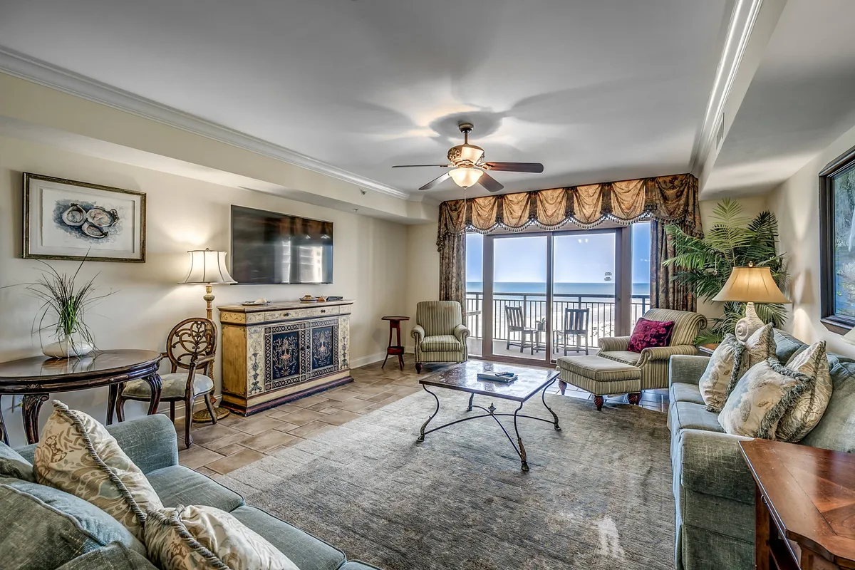 A bright, spacious living area featuring plush seating arranged to take in stunning ocean views through expansive windows, with tasteful coastal decor, a cozy lamp, and an inviting side chair by the window—perfect for relaxing, reading, or gathering with family and friends.