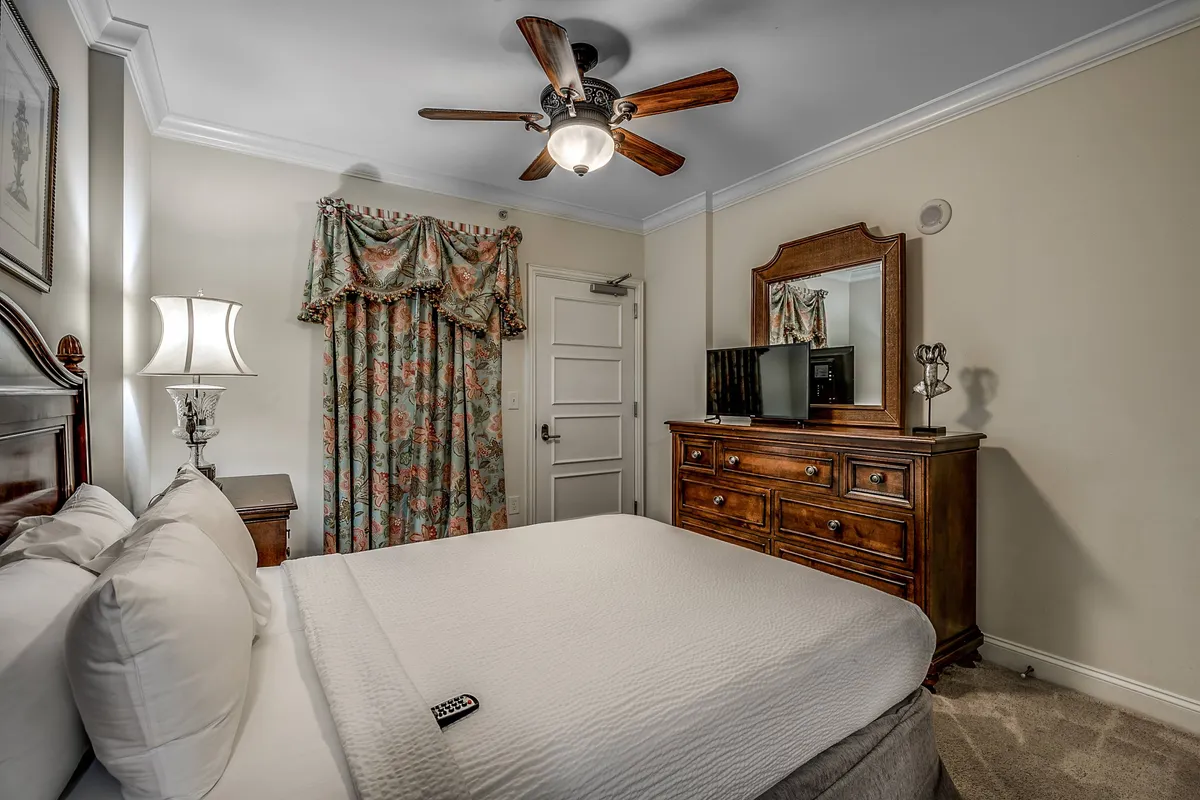 A cozy bedroom scene featuring a comfortable bed, dresser, soft lighting from a lamp, and sunlight streaming through the curtains. The tranquil space highlights relaxation and personal comfort, key elements for a resort-like stay.