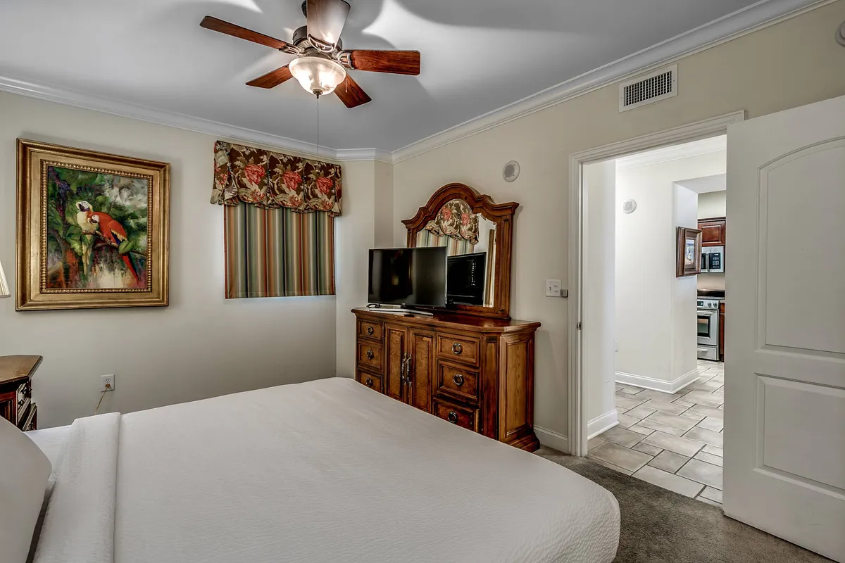 A tastefully decorated bedroom featuring a wooden dresser, a modern television, and a painted parrot artwork. The bed sits nearby, making this a cozy environment perfect for unwinding with a show or a book.