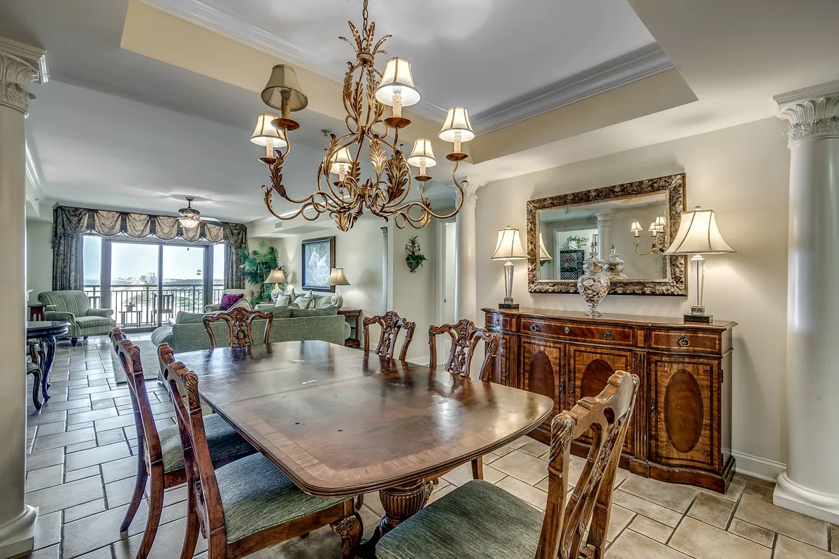 This image highlights a large dining table under a chandelier, adjacent to a sofa area and decorative mirror. The scene conveys a warm, inviting mood, perfect for family dinners, entertaining guests, and sharing special occasions.