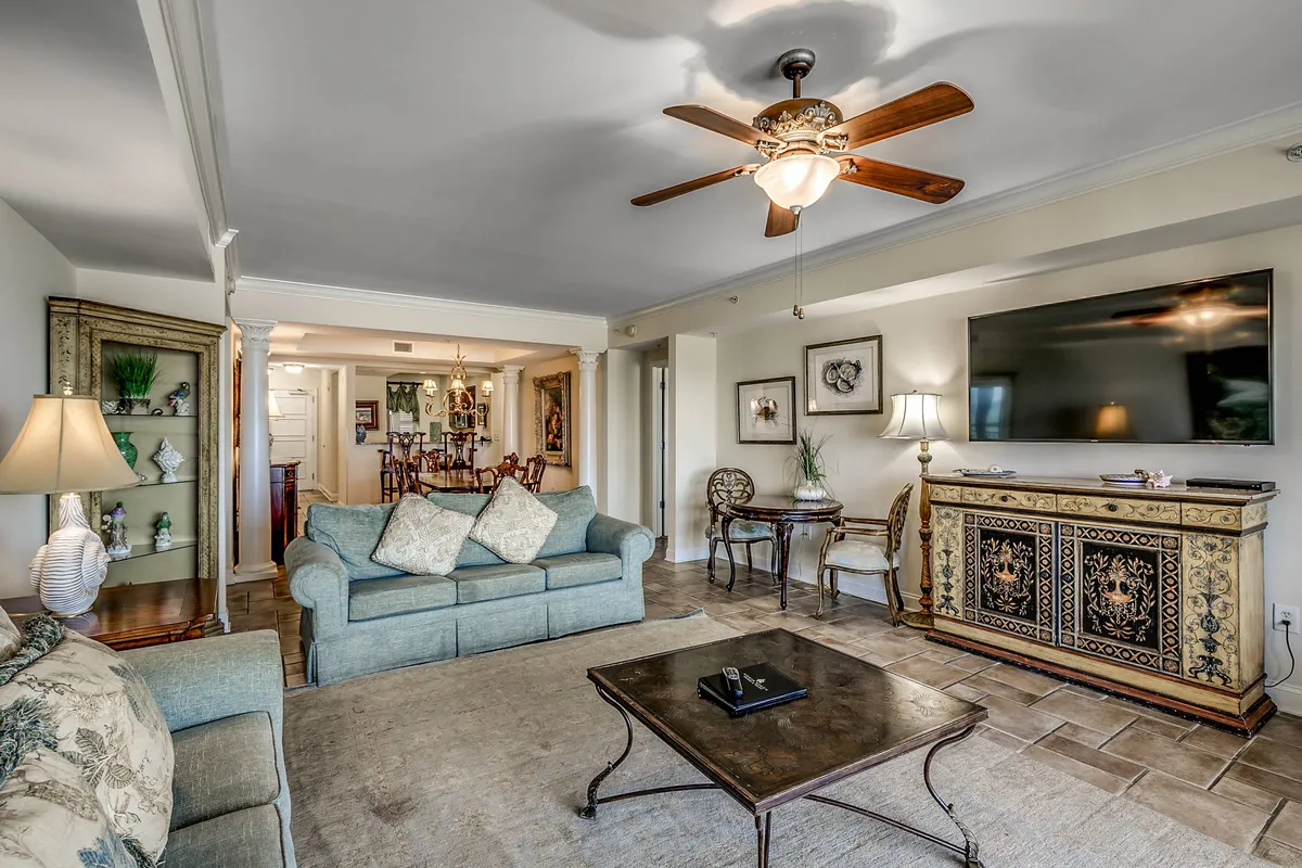This image features a spacious and inviting living room with a comfortable sofa adorned with decorative pillows, an ornate cabinet, a large television, and a coffee table. The arrangement suggests a space ideal for both relaxing and entertaining guests, with a layout that encourages social interaction and group activities.