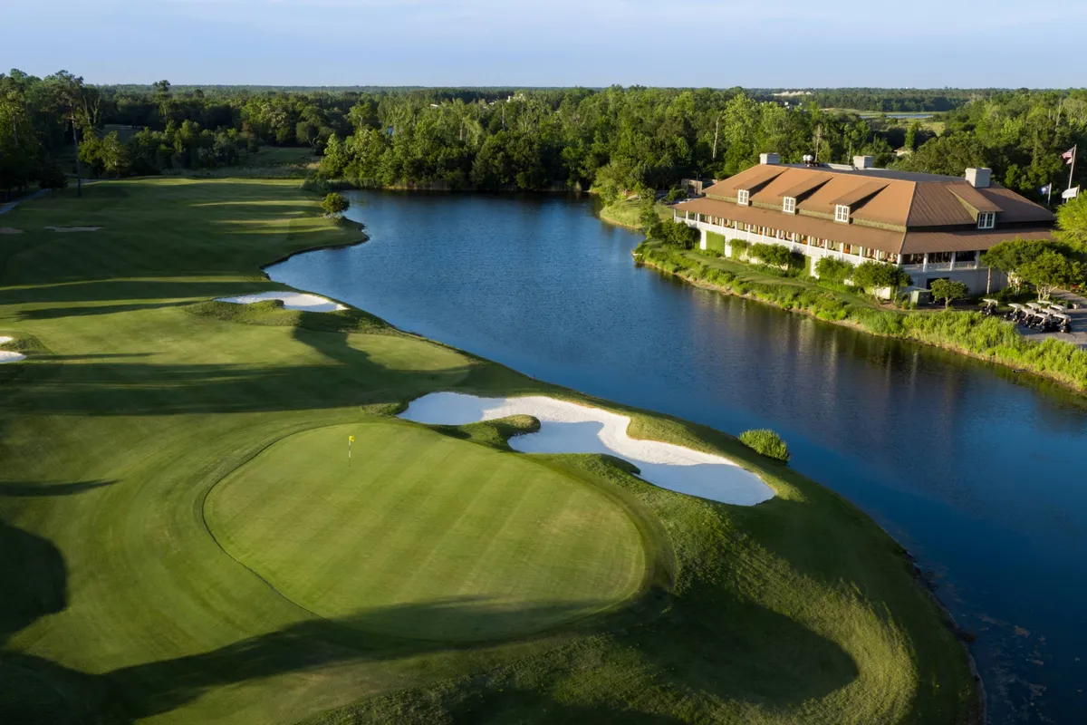 A picturesque view of the Azalea Sands Golf Club, showing the lush fairways alongside a tranquil lake and the welcoming clubhouse. The scene is peaceful yet inviting, perfect for a group golf outing or post-game relaxation.